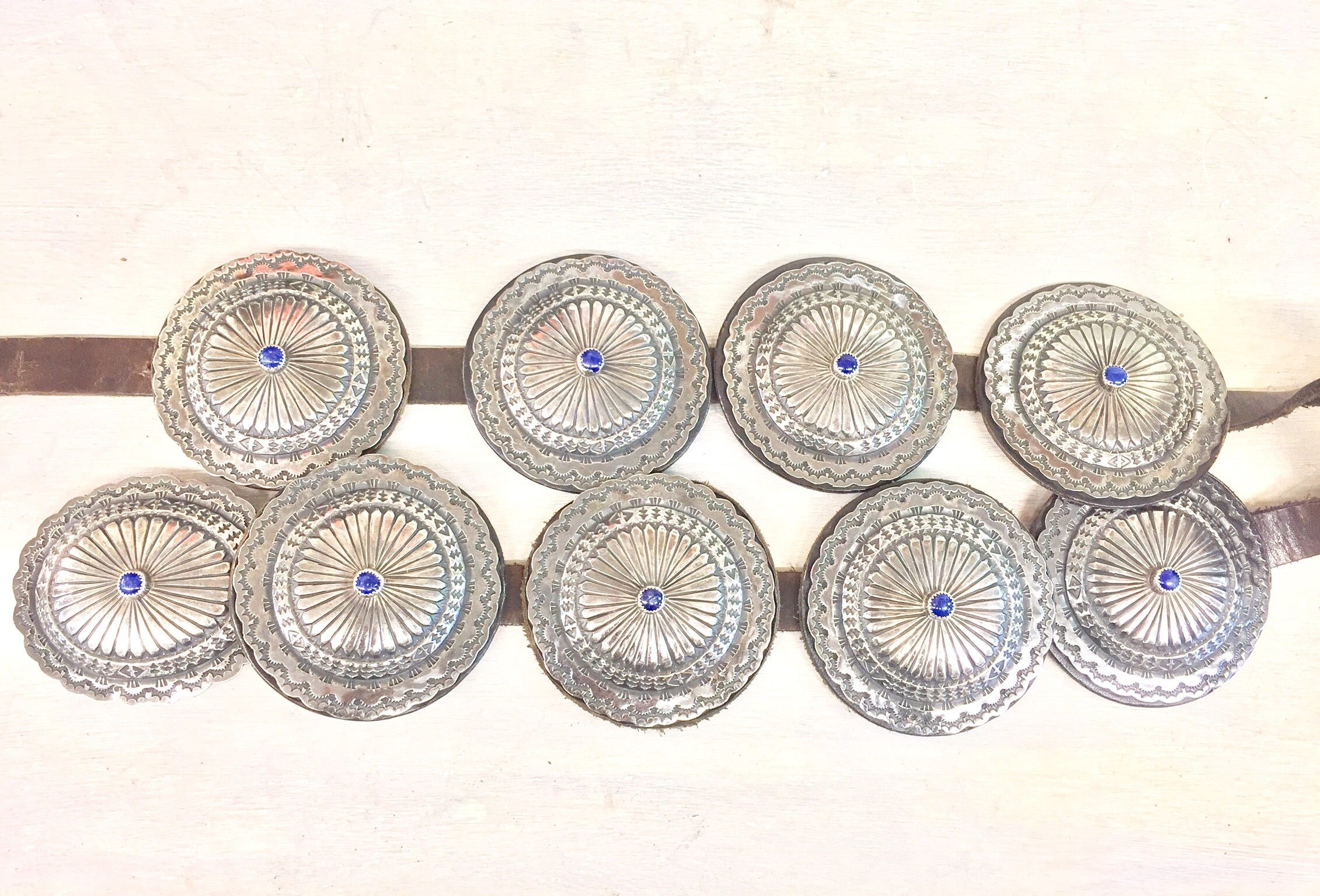 Vintage Navajo sterling silver concho belt with ornate hand-stamped conchos featuring central lapis lazuli stones set on a brown leather strap, an authentic Native American southwestern accessory.