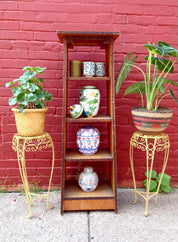 Antique wooden shelf with decorative metal plant stands and various colorful ceramic pots against a vibrant pink brick wall.