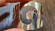 Vintage sterling silver Reed and Barton cuff bracelet with swirl design, held in hand against wooden surface