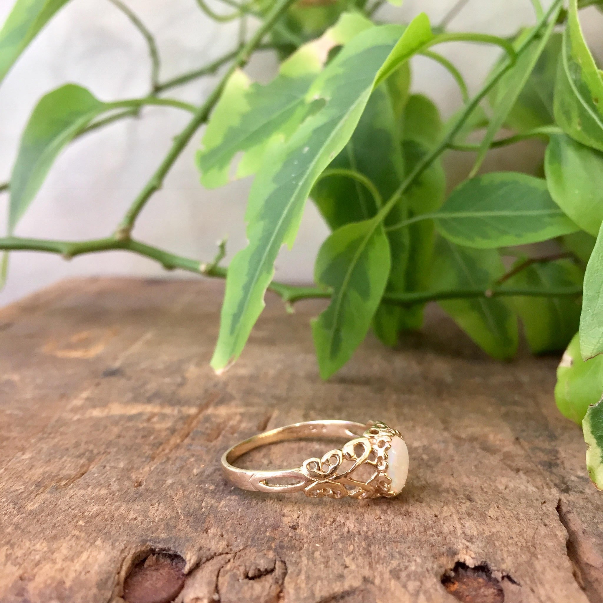 Vintage 10K yellow gold filigree ring with opal gemstone on weathered wood surface with green foliage in background