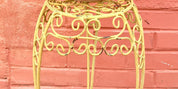 Ornate yellow metal plant stand against a coral pink brick wall