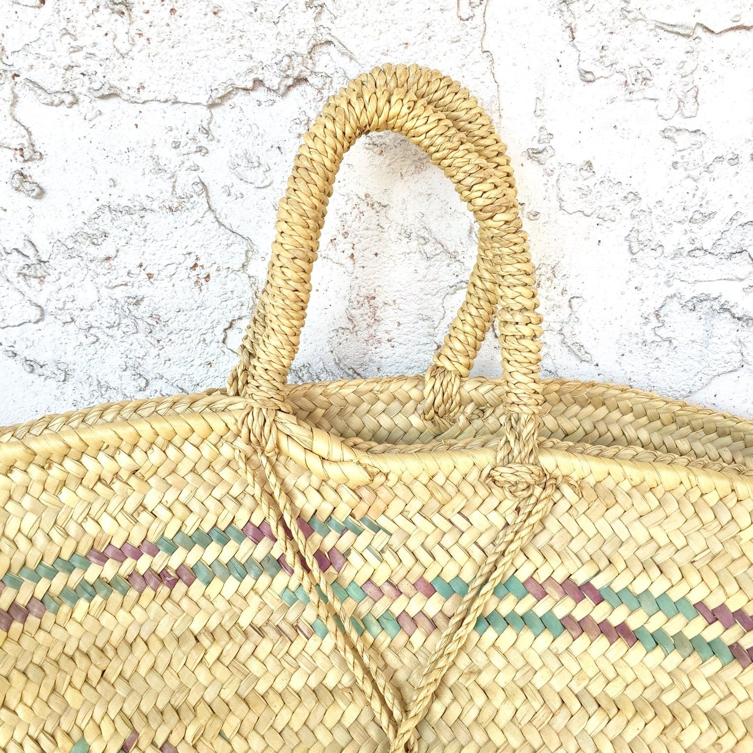Handwoven straw beach bag with bohemian boho style details against a textured white wall, perfect as a handmade gift for her.