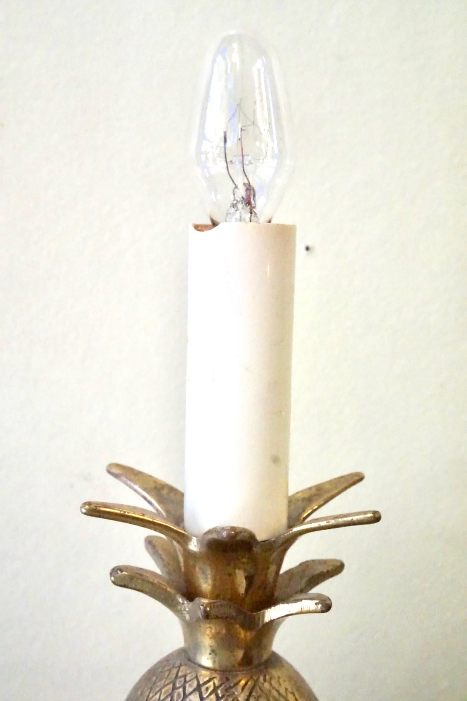 Vintage brass pineapple-shaped table lamp with illuminated candle-like bulb, providing bohemian accent lighting and decor for the home.