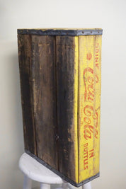 Vintage wooden Coca-Cola bottle crate with faded yellow paint and aged patina