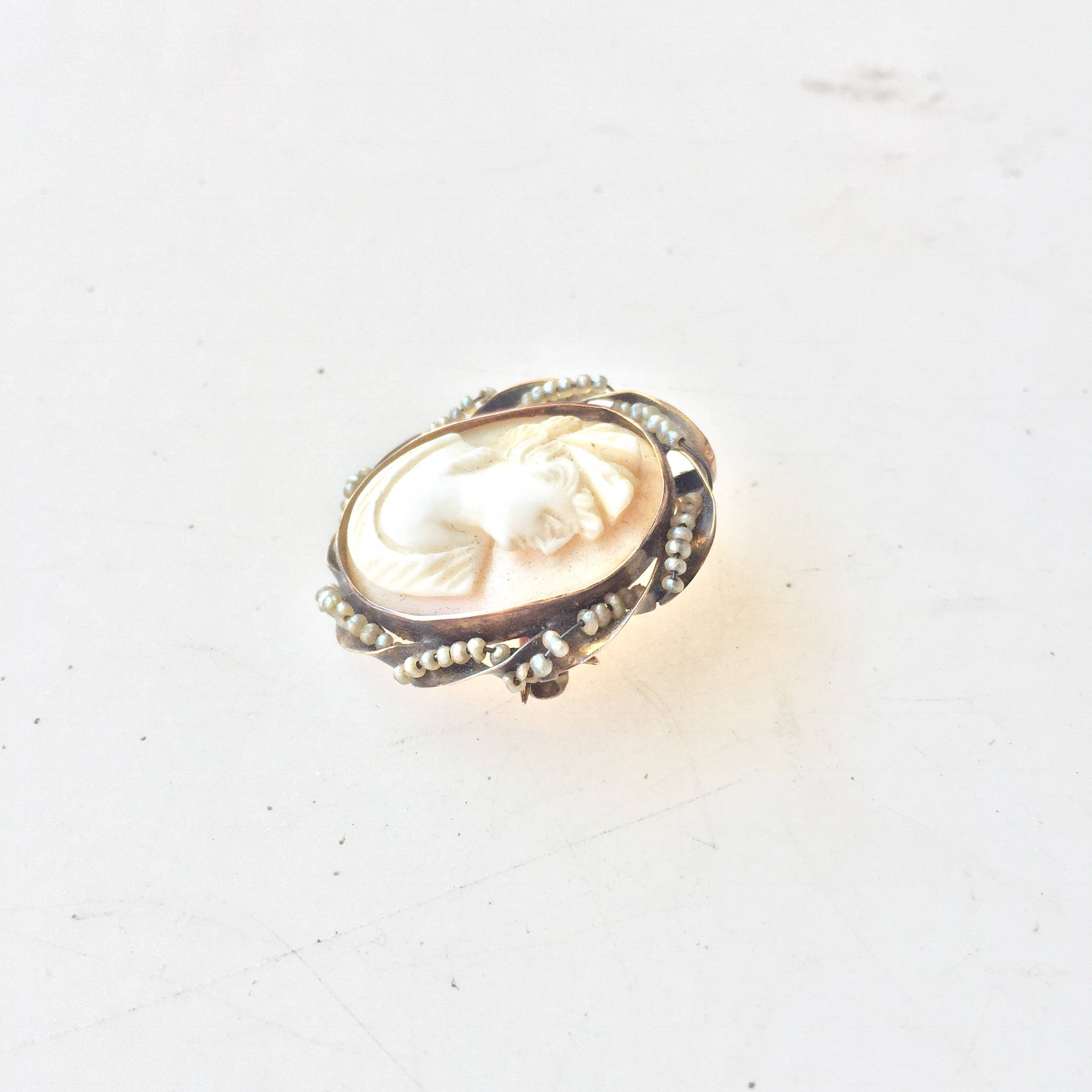 Antique 10 karat gold cameo brooch or pendant featuring a detailed carved shell cameo set in an ornate gold frame with beaded border, photographed on a plain white background.