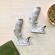 Vintage pewter fish-shaped candlestick holders on wooden surface next to antique book, suitable as housewarming or holiday gift idea for home decor.