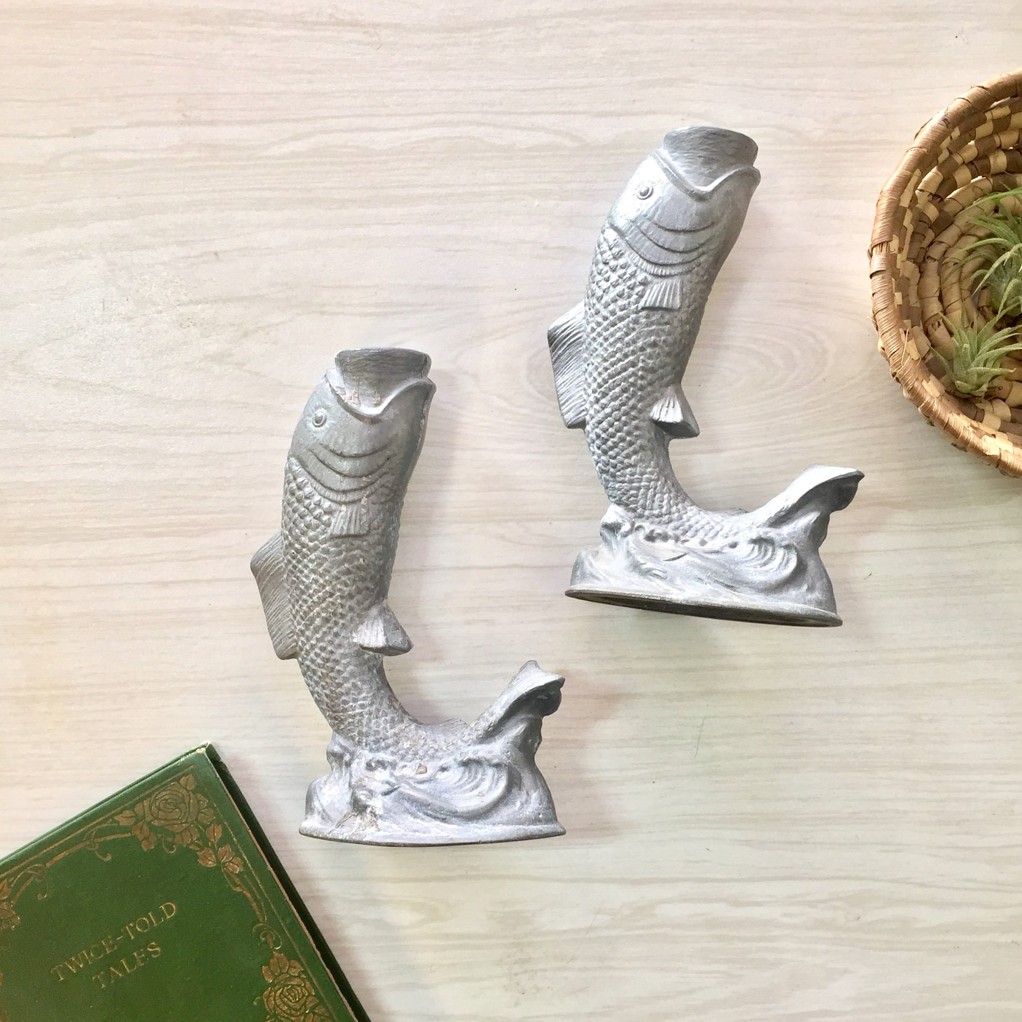 Vintage pewter fish-shaped candlestick holders on wooden surface next to antique book, suitable as housewarming or holiday gift idea for home decor.