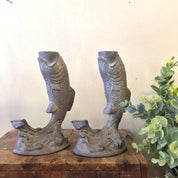 Vintage pewter fish shaped candlestick holders on wooden surface with greenery in background