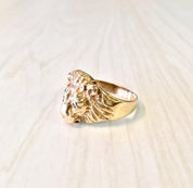 Vintage 10K gold lion head ring with diamond accents, a bold statement piece featuring intricate detailing of a fierce lion's head crafted in yellow gold with glittering diamond eyes, displayed on a light wood surface.