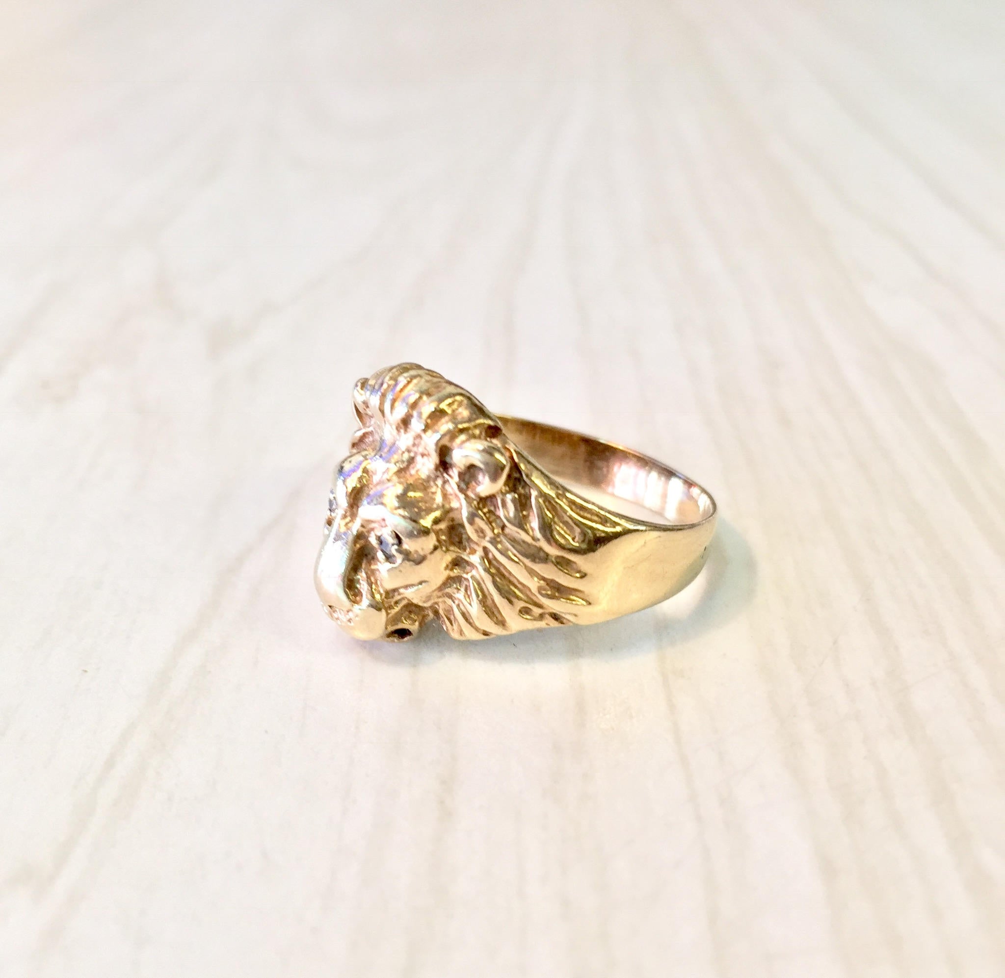 Vintage 10K gold lion head ring with diamond accents, a bold statement piece featuring intricate detailing of a fierce lion's head crafted in yellow gold with glittering diamond eyes, displayed on a light wood surface.