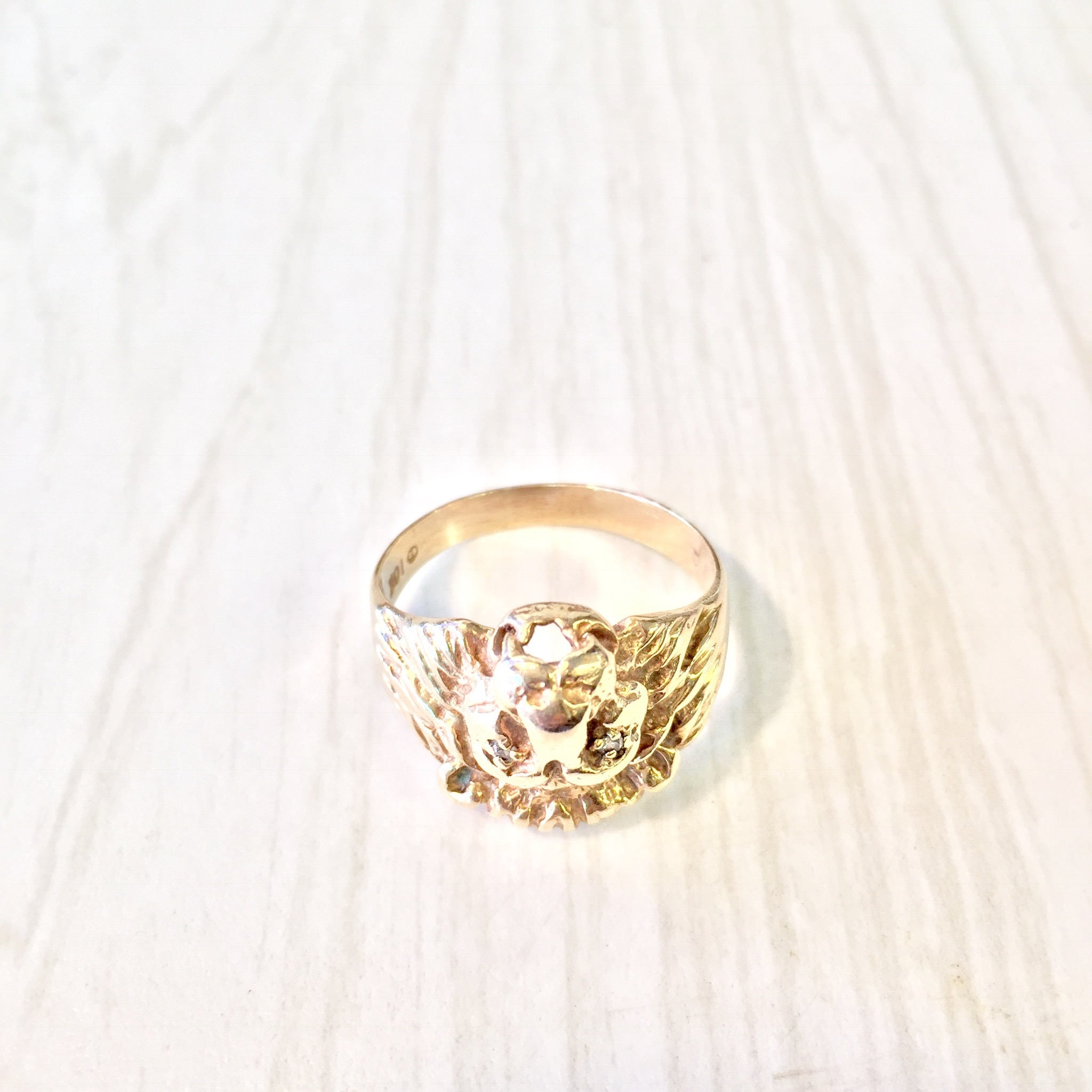 Vintage 10K gold lion head ring with diamond accents on a white wooden background