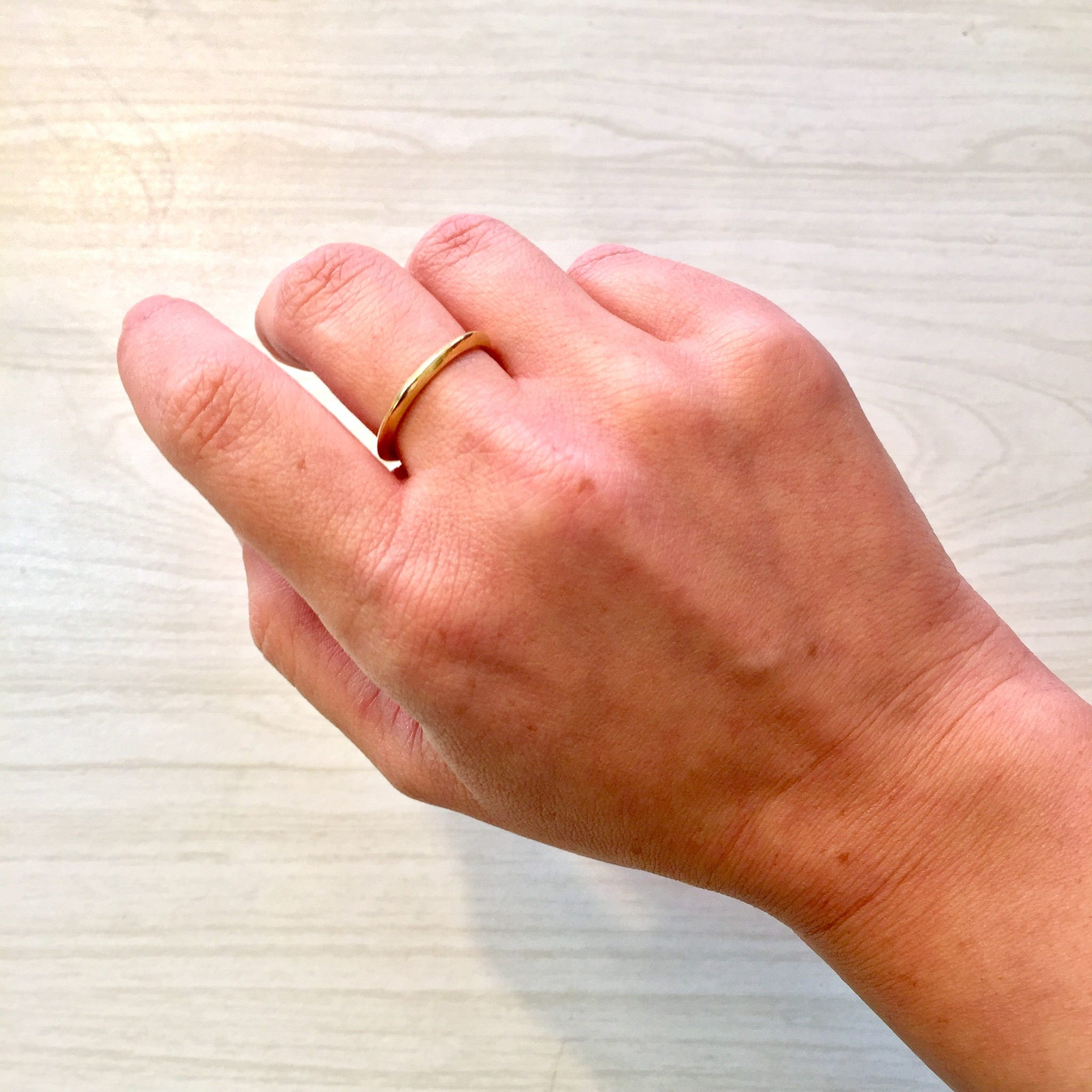 18K yellow gold stacking ring on a hand, showing a simple, skinny gold wedding band.