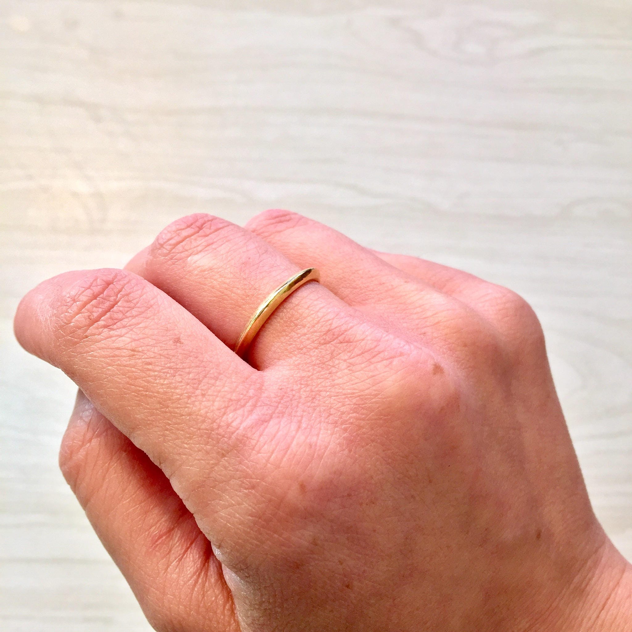18K yellow gold stacking ring on a hand, showing a simple skinny gold wedding band worn on the ring finger.