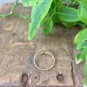 Fresh green plant leaves and stems on a rustic wooden surface, with a delicate vintage gold filigree ring with small opal stones placed in the foreground.