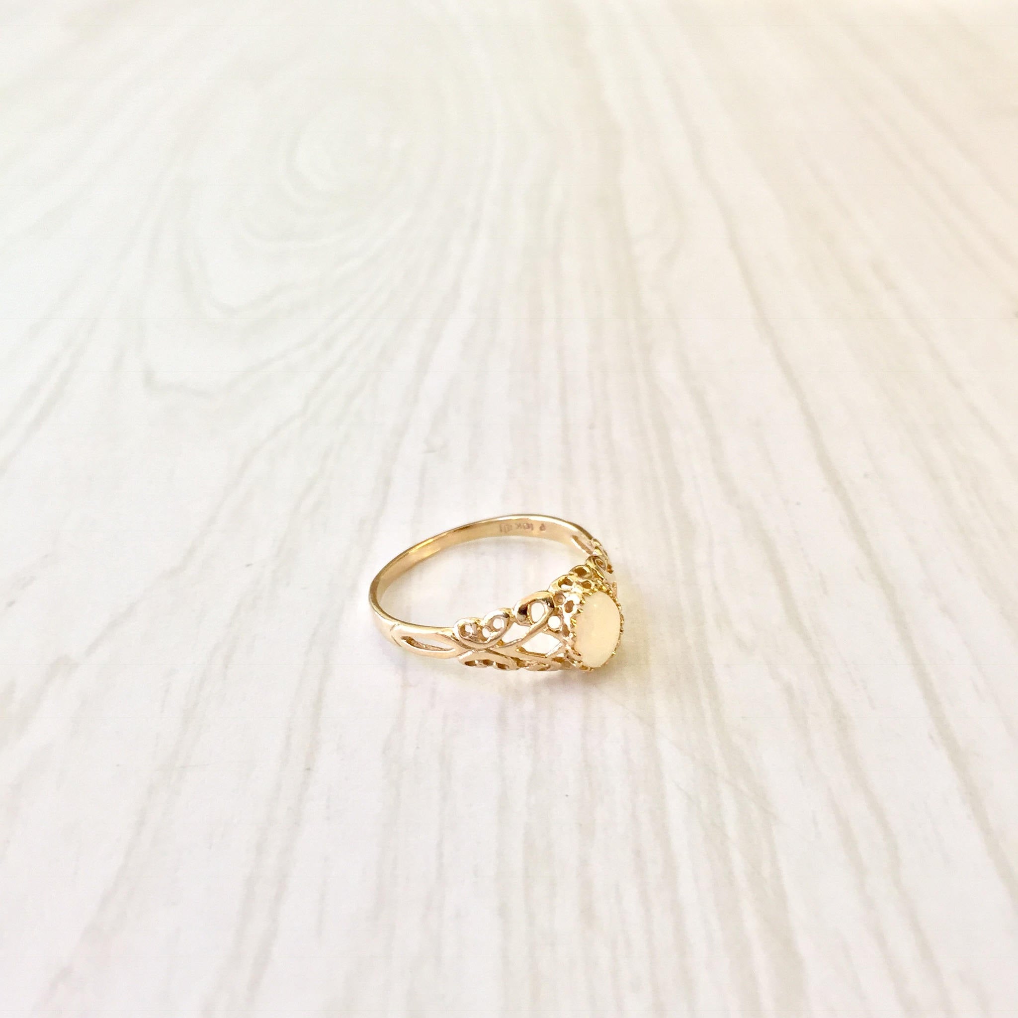 10K yellow gold filigree ring with opal stone on light wooden background, vintage Art Deco style engagement or promise ring, gift idea for her