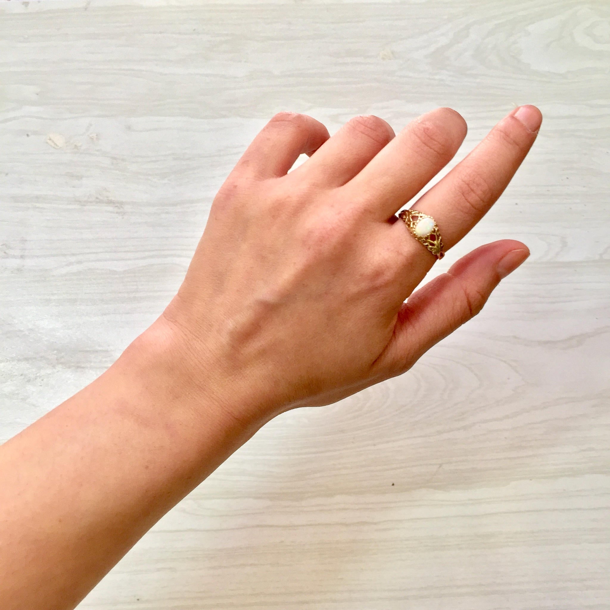 Vintage 10K yellow gold filigree ring with opal gemstone on a hand, against a light wood background.