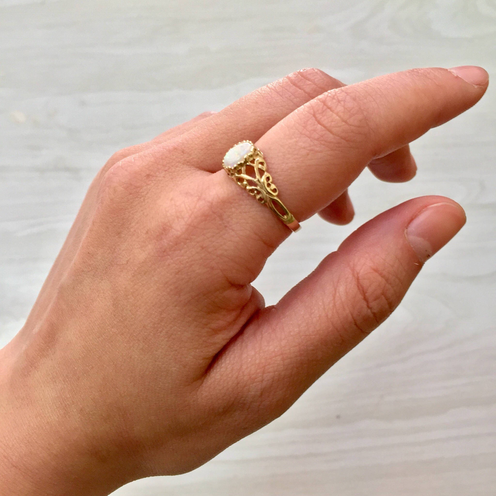 Vintage 10K yellow gold filigree ring featuring a round opal gemstone, shown on a hand against a light background.