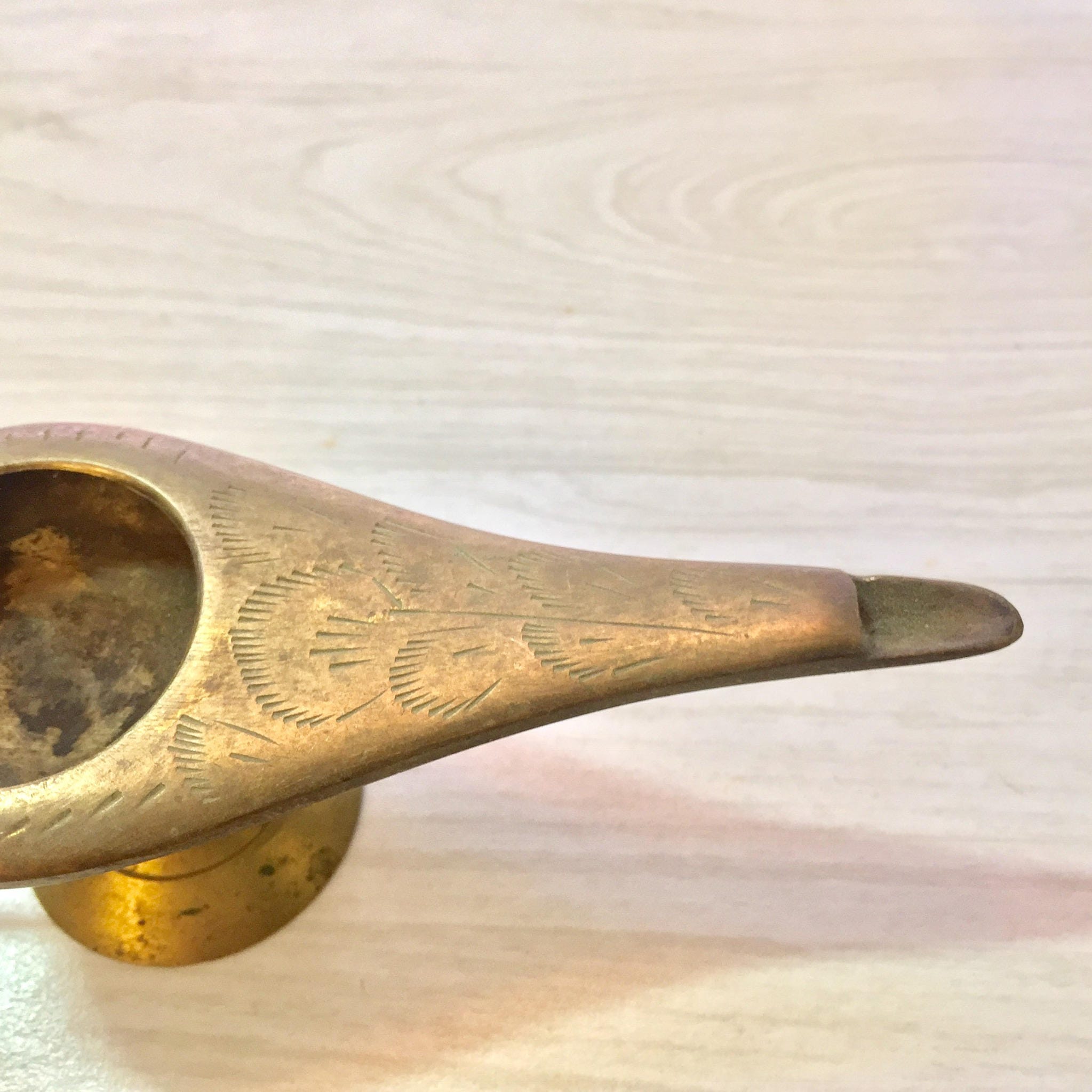 Vintage etched brass genie lamp shaped incense burner or oil pitcher, with detailed engraved patterns, lying on a light colored fabric surface.