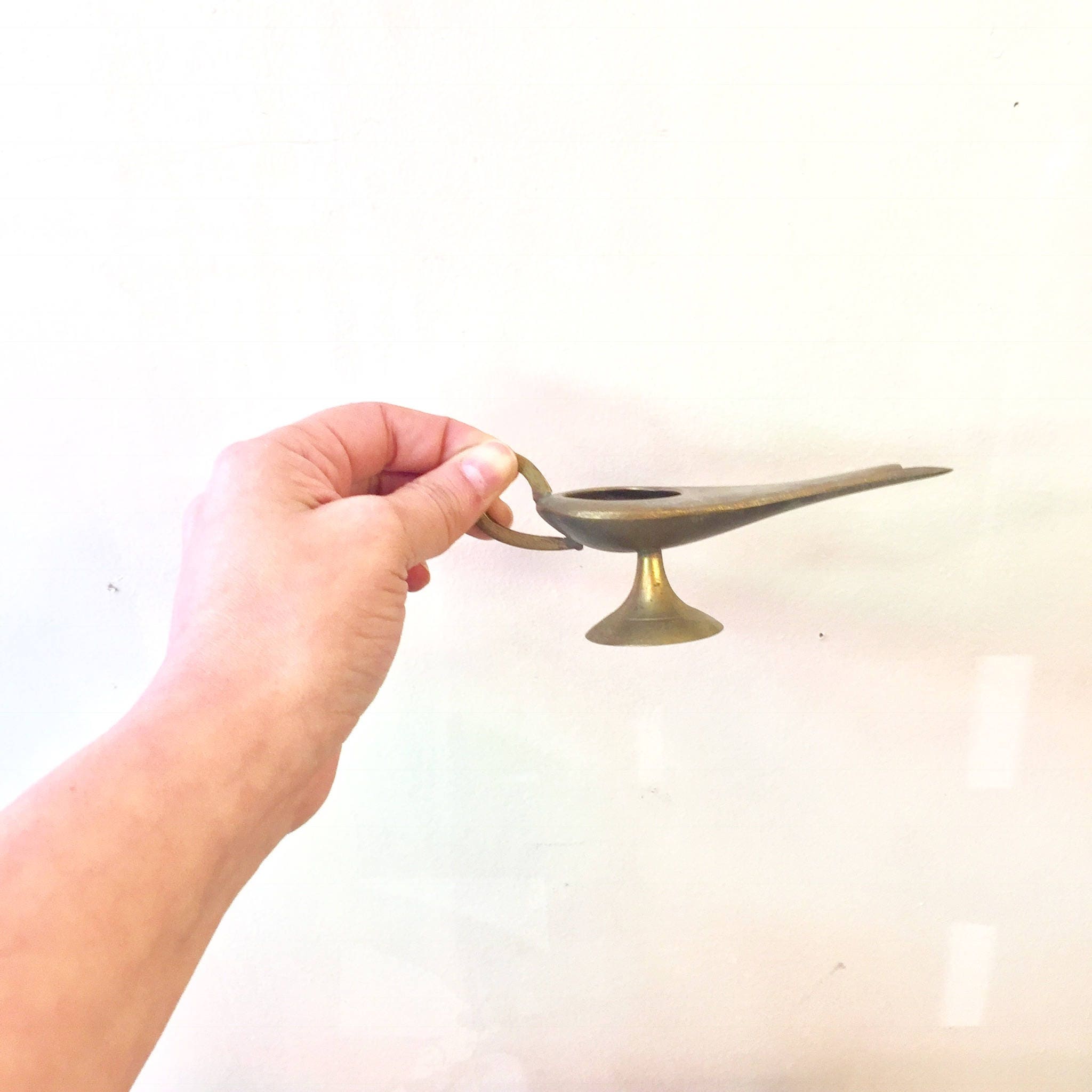 Vintage brass genie lamp incense burner held in hand against white background