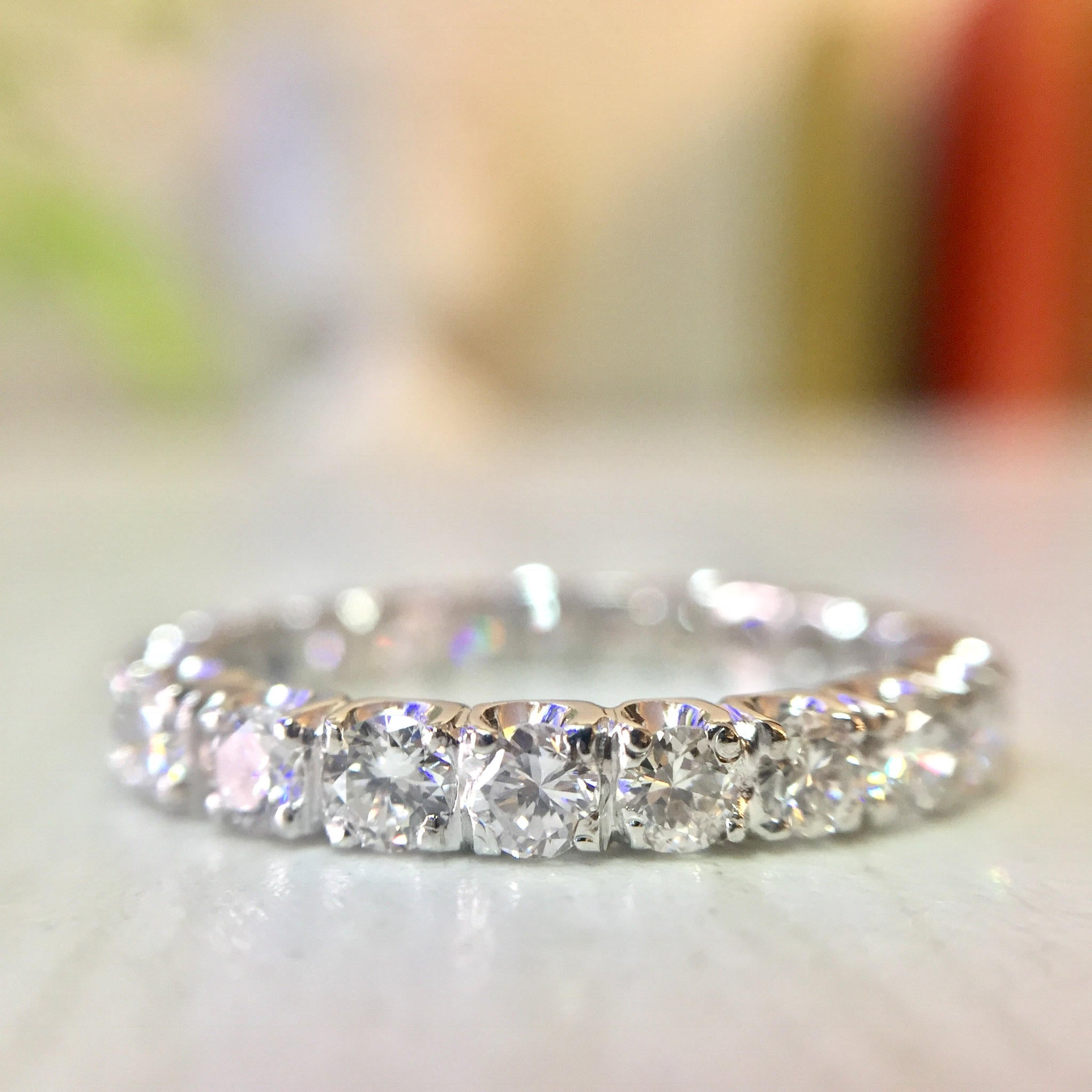 14 Karat White Gold Diamond Eternity Wedding Band with Round Brilliant Cut Stones on Blurred Background