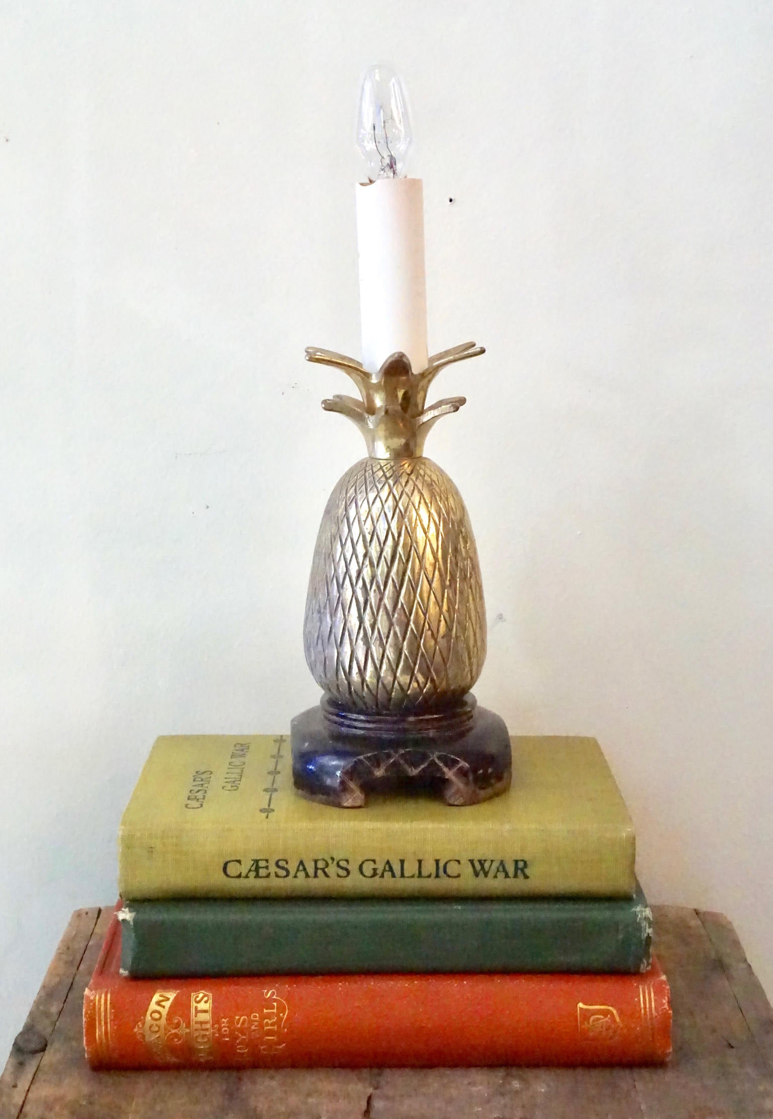 Vintage brass pineapple-shaped table lamp on stack of antique books, serving as a unique bohemian home decor accent or gift