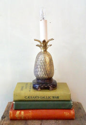 Vintage brass pineapple-shaped table lamp on stack of antique books, serving as a unique bohemian home decor accent or gift