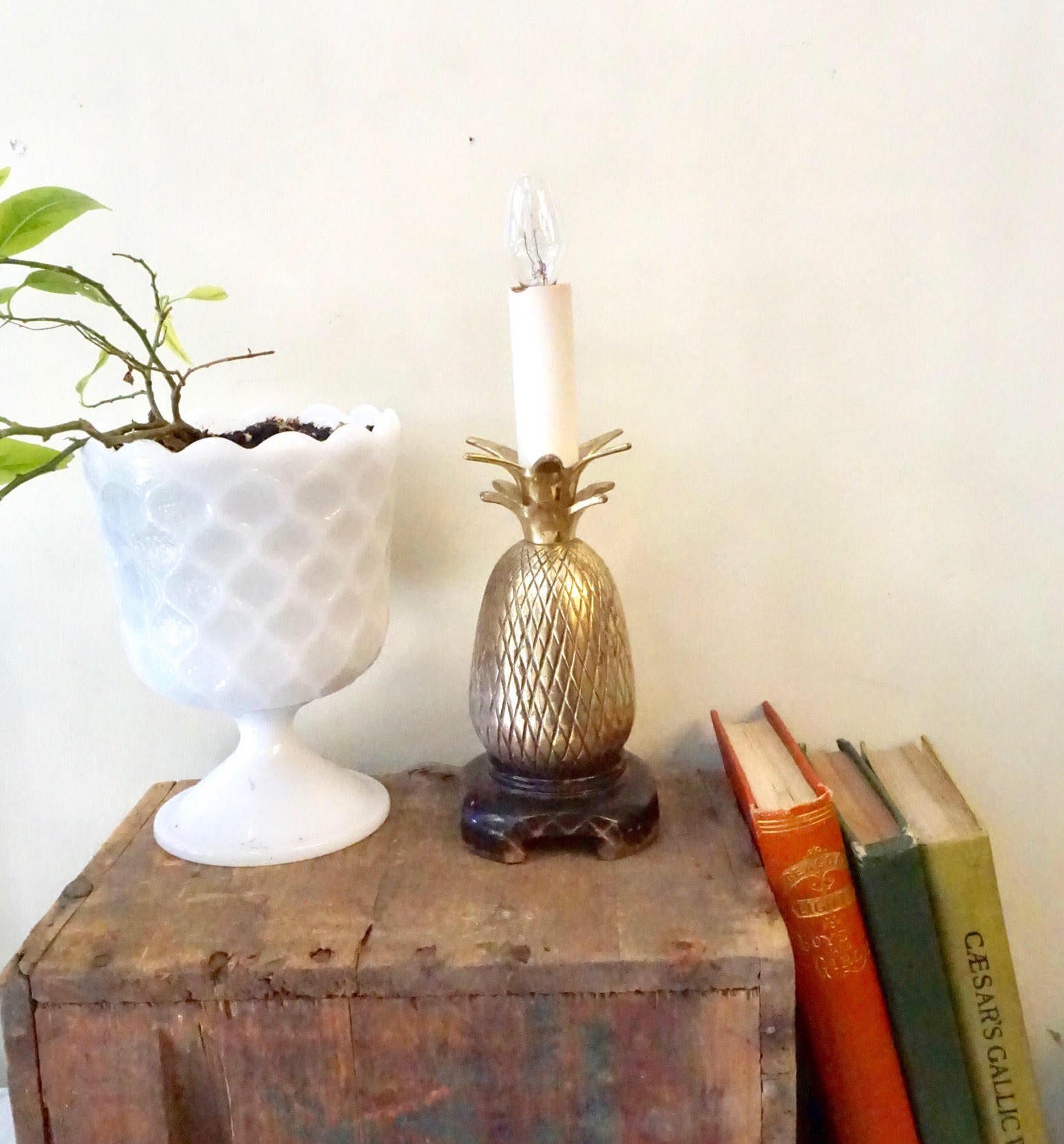 Vintage brass pineapple lamp on wooden table next to white vase and books, bohemian home decor accent lighting