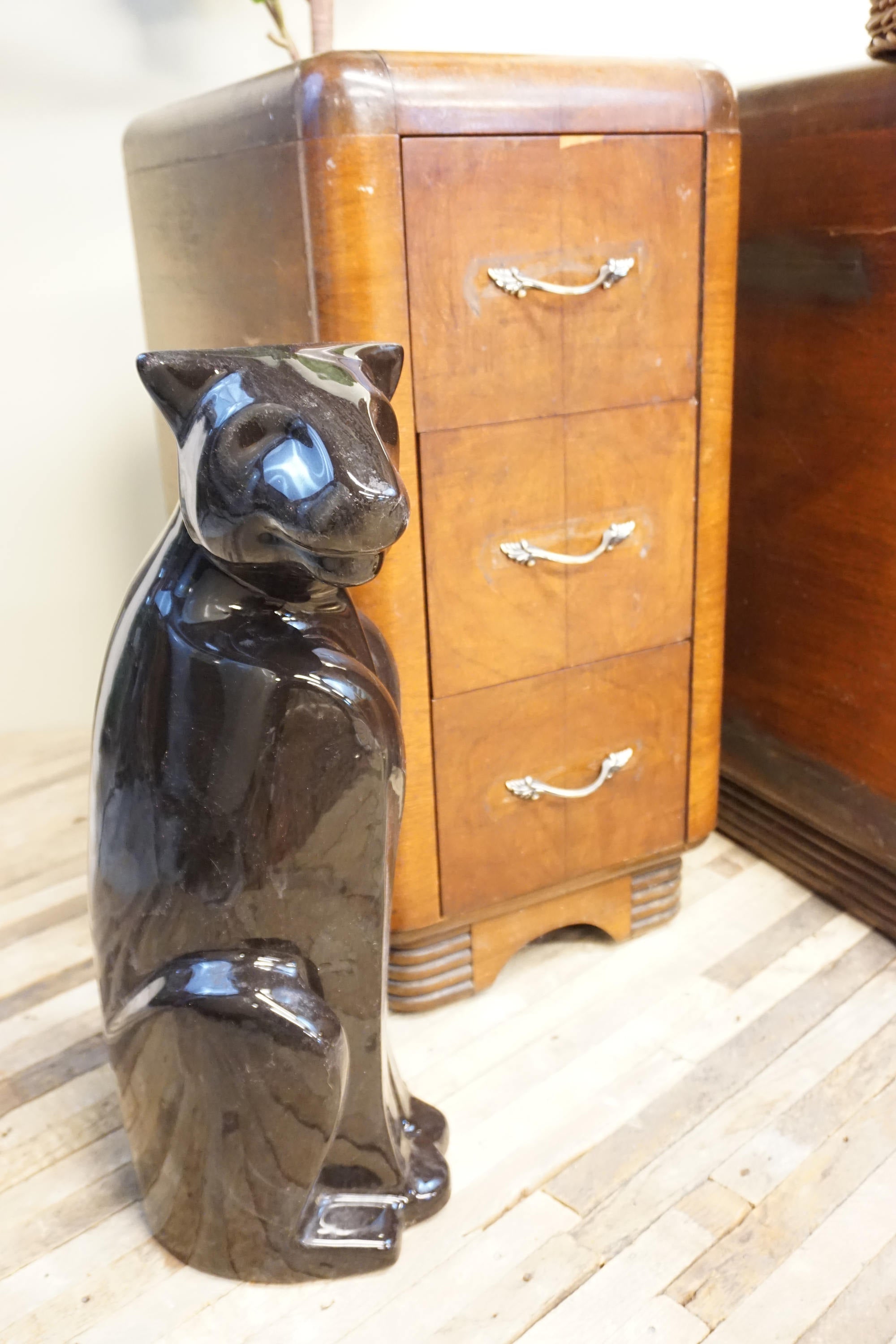 Large black ceramic panther statue next to wooden cabinet with drawers. The glossy panther figurine stands upright and has blue accents.