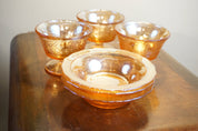 Set of four vintage orange iridescent carnival glass dessert dishes on a wooden table, the glass bowls have a swirled, textured pattern that catches the light