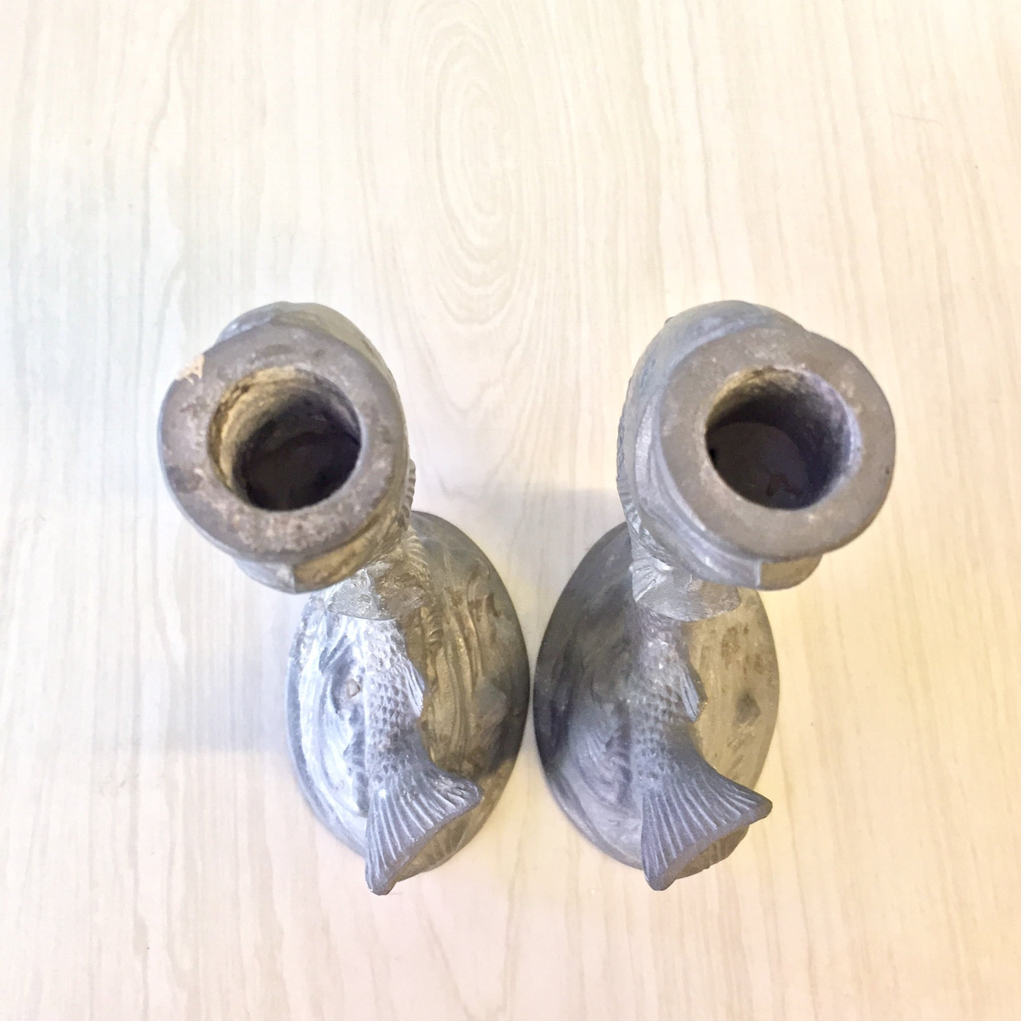 Pair of vintage pewter fish-shaped candlestick holders on wooden surface, antique home decor