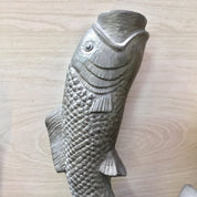 Vintage pewter fish-shaped candlestick holder with textured scales and fins, sitting upright on a wooden surface.