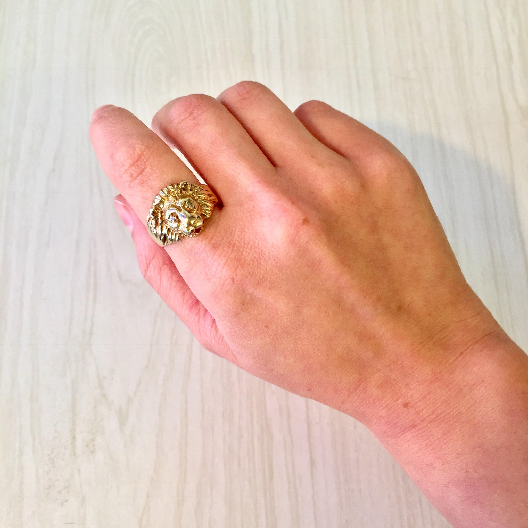 Close-up of a hand wearing a vintage 10 karat gold ring featuring a lion's head design accented with small diamonds, resting on a white wooden surface.