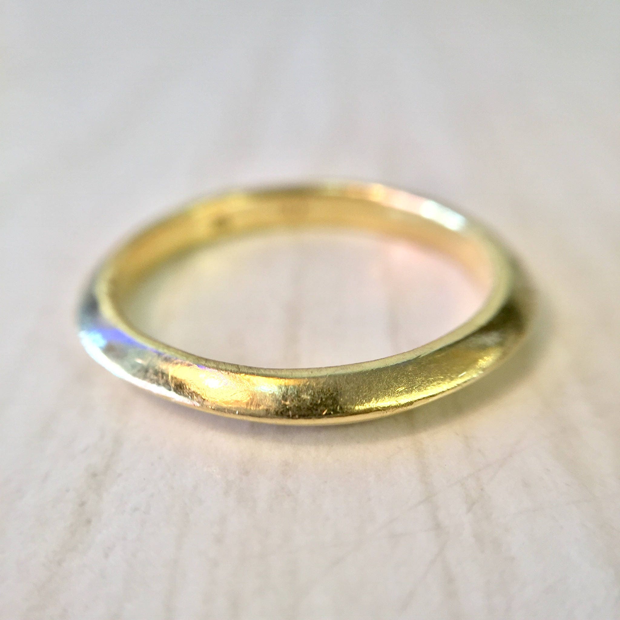 18K yellow gold thin, simple stacking ring or wedding band with a sleek, polished finish, shown close-up on a light background.