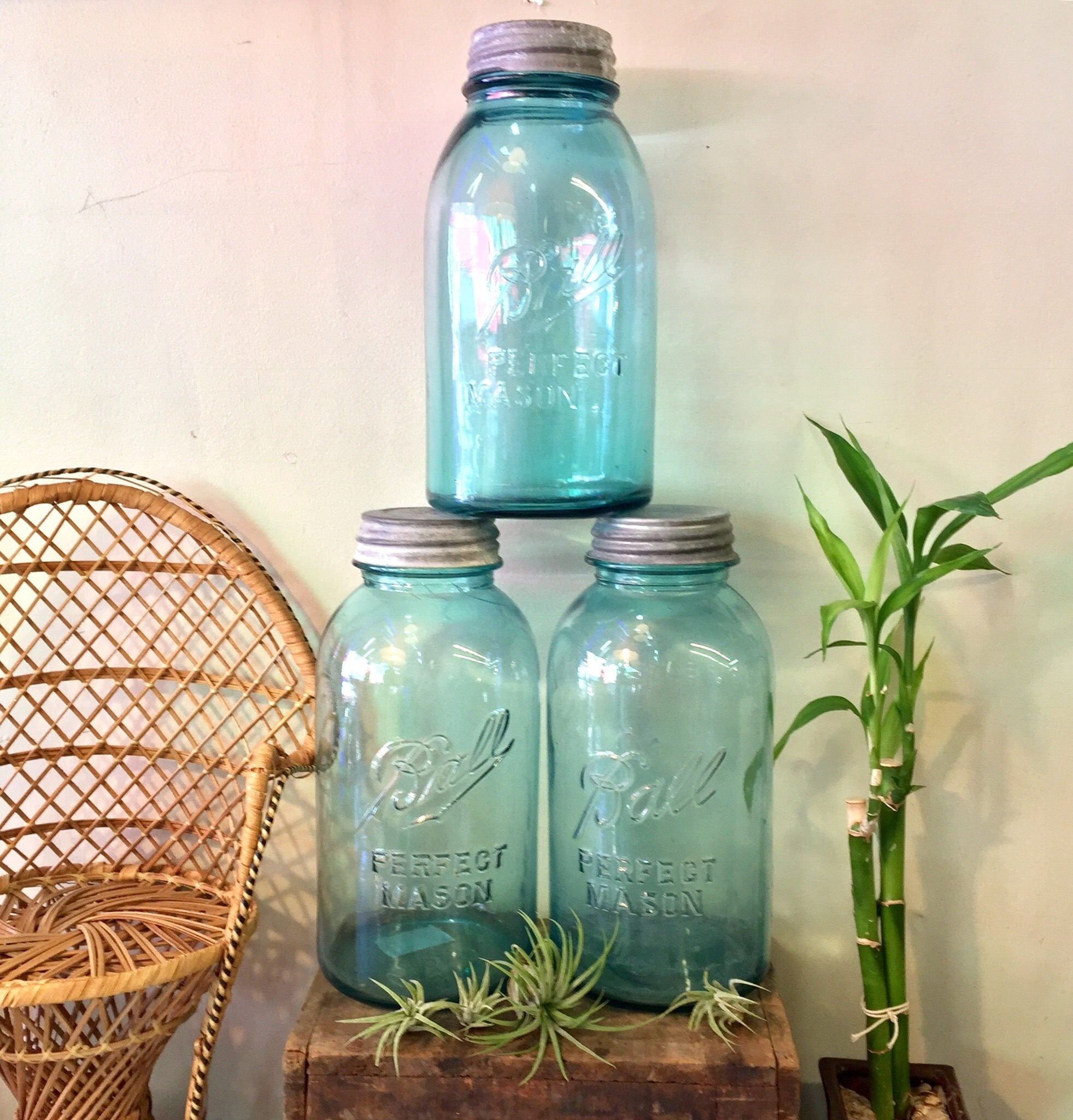 Set of three antique blue Ball Mason jars with zinc lids on wooden surface with wicker chair and plants in background