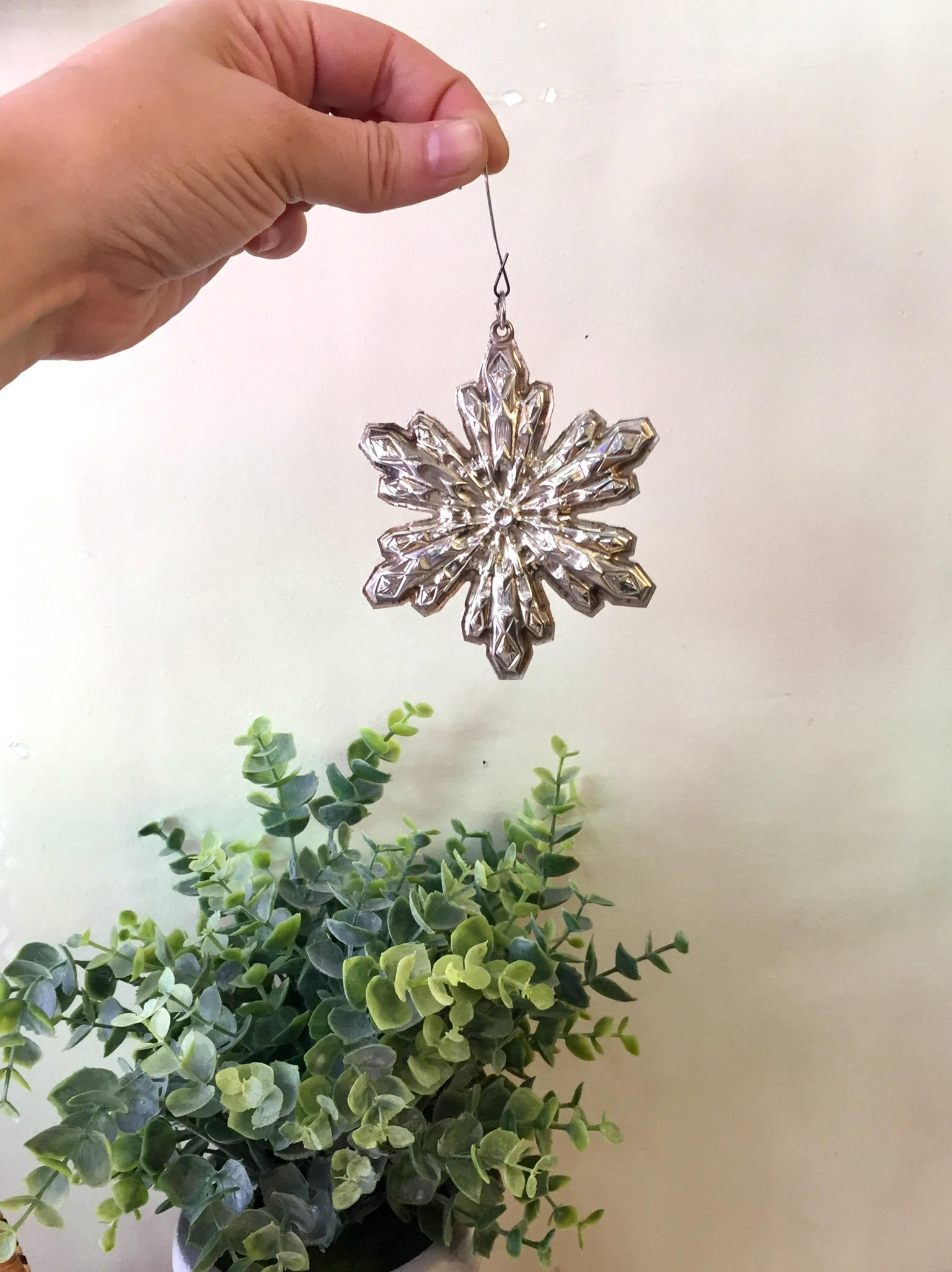 Hand holding a vintage Sterling silver Gorham snowflake Christmas ornament with greenery in the background