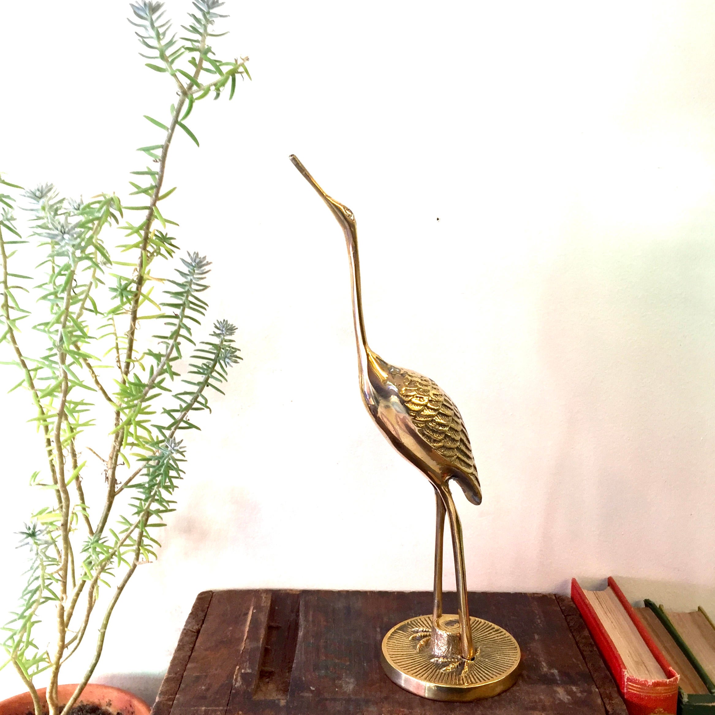 Vintage brass crane statue on wooden table with plant and books