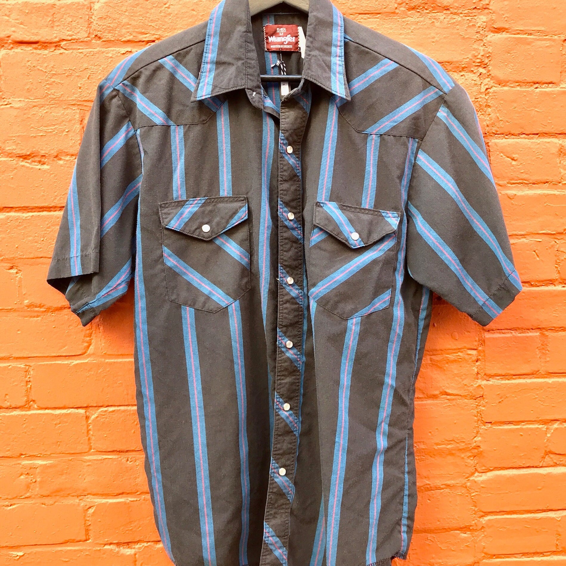 Vintage Wrangler striped western shirt with short sleeves and snap buttons hung on brick wall