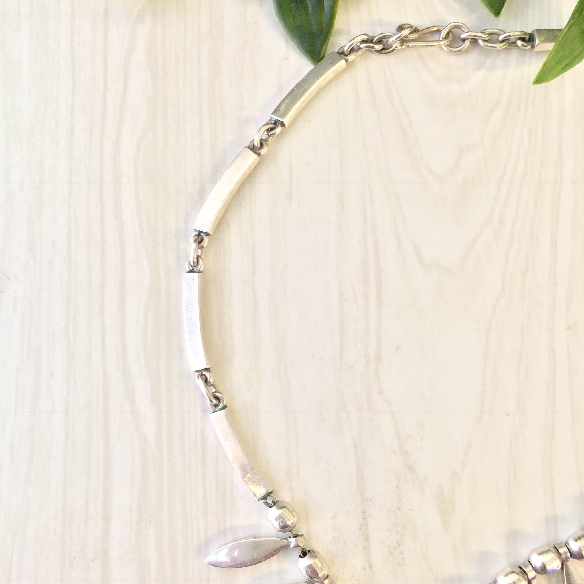 Vintage sterling silver statement necklace with white beads and green leaves on a light wooden background