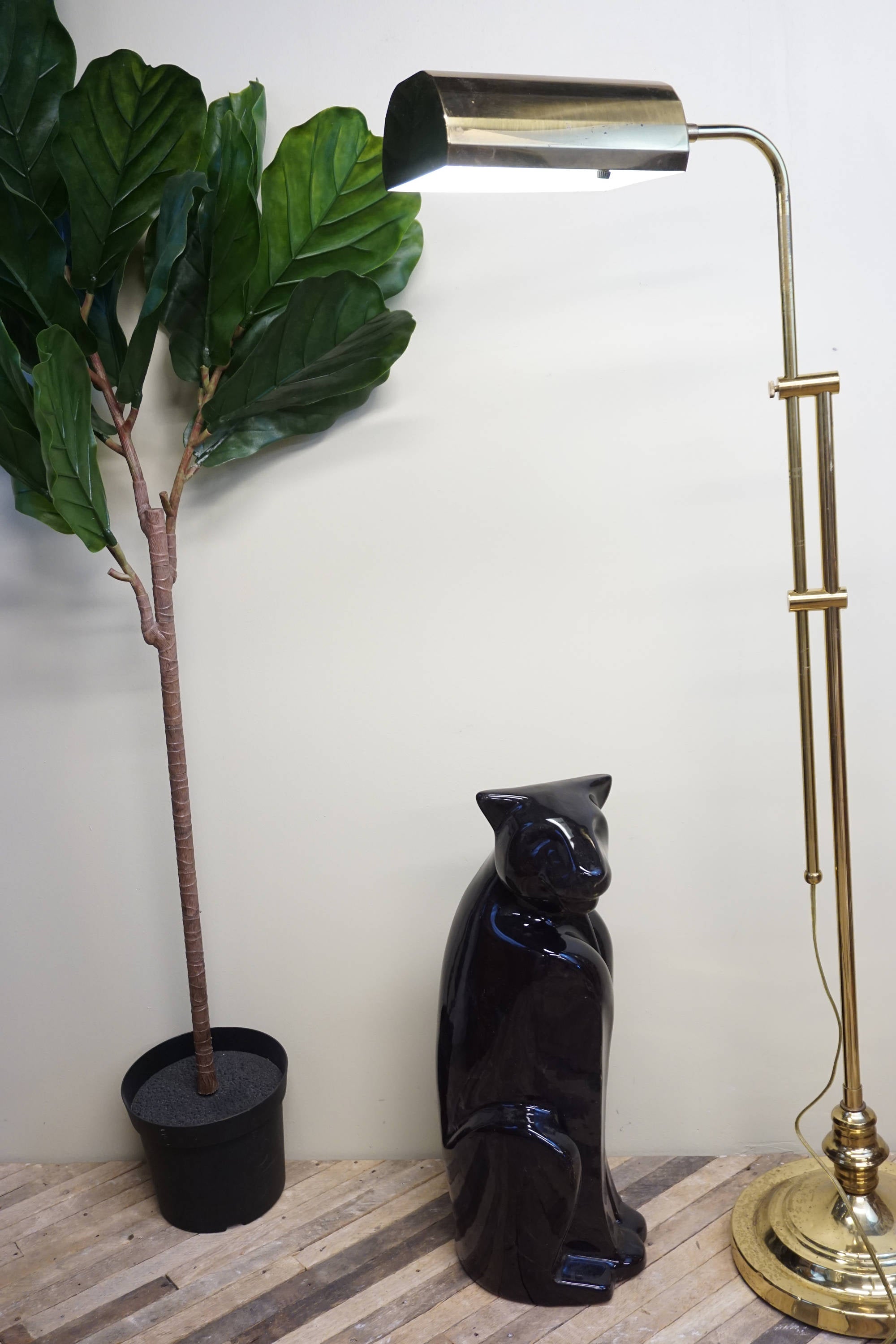 Tall vintage brass floor lamp with adjustable shade alongside a large dark blue ceramic Royal Haeger panther statue and a potted green plant, against a plain white wall and wooden floor.
