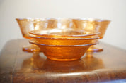 Set of three vintage orange carnival glass dessert dishes with an iridescent sheen, stacked on a wooden surface