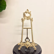 Vintage brass filigree easel book holder stand on black marble base with green leaf in background