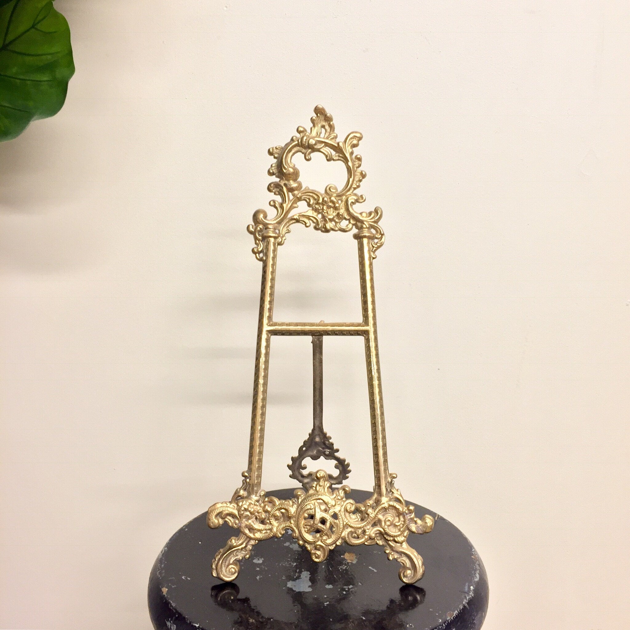 Vintage brass filigree easel book holder stand on black marble base with green leaf in background