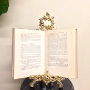 Vintage brass filigree easel book stand holding open an old book, used as decorative home decor piece.