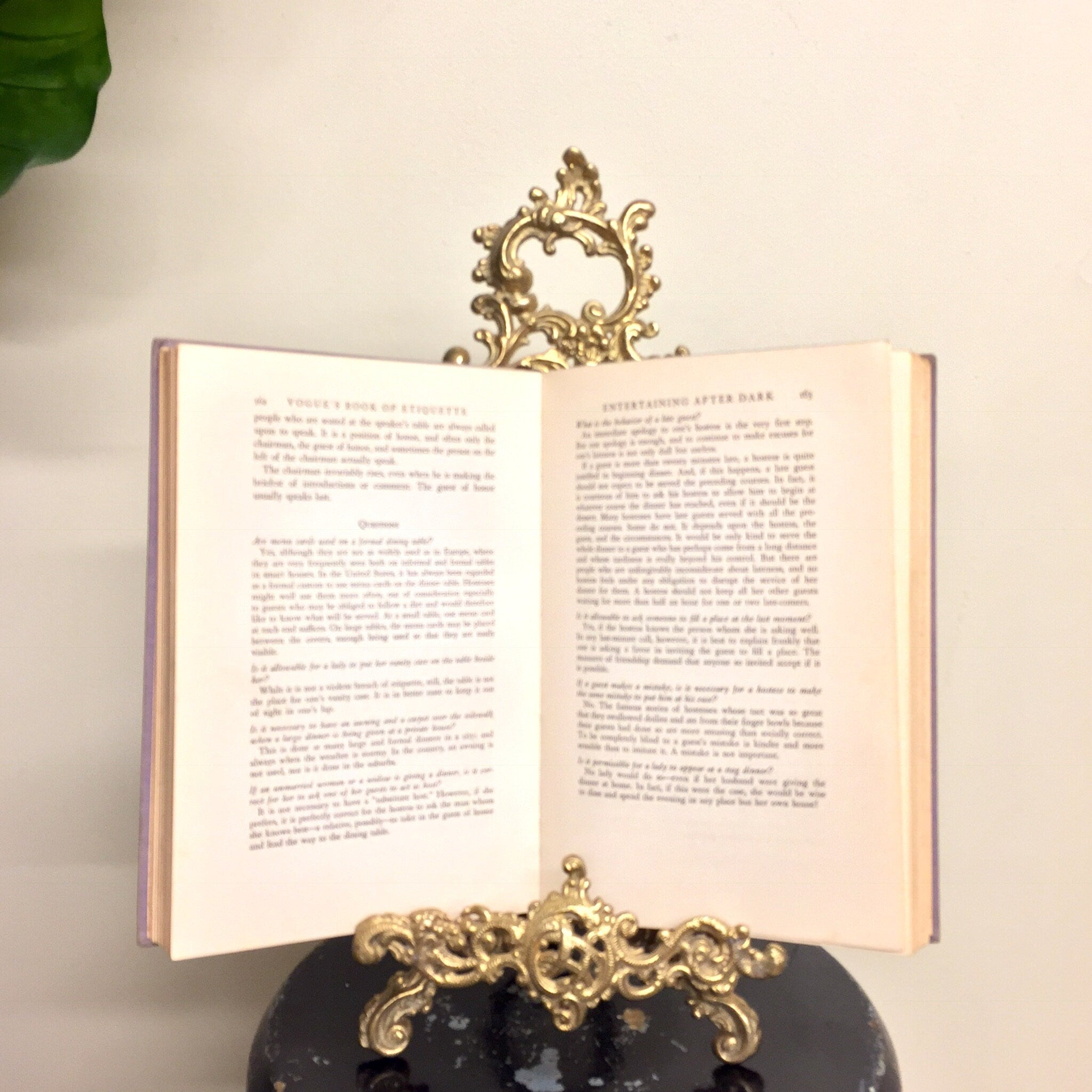 Vintage brass filigree easel book stand holding open an old book, used as decorative home decor piece.