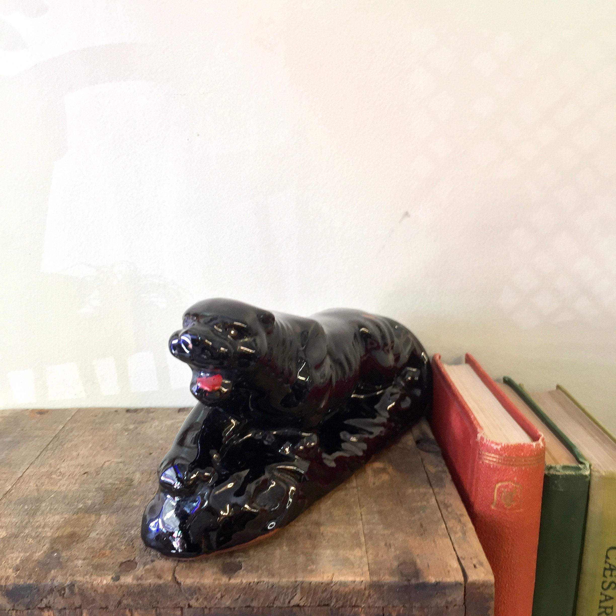 Vintage black ceramic panther figurine or statue, made in Japan, positioned on wooden surface next to old books, suitable as home decor for a mantle piece or bookcase, an ideal gift for a cat lover or collector.