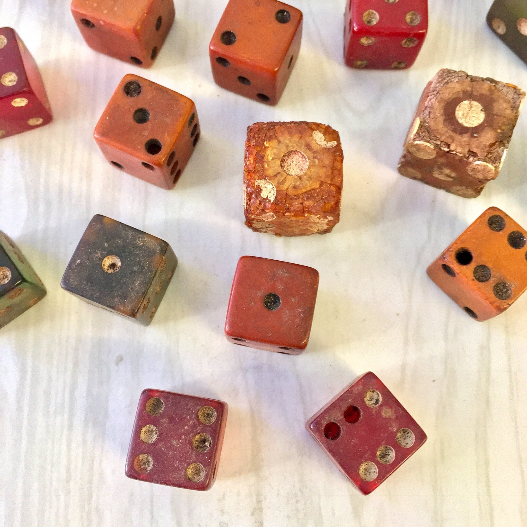 Antique wooden dice in assorted colors and sizes, some with gold painted dots, scattered on a white textured surface, suitable for vintage games or arts and crafts projects.