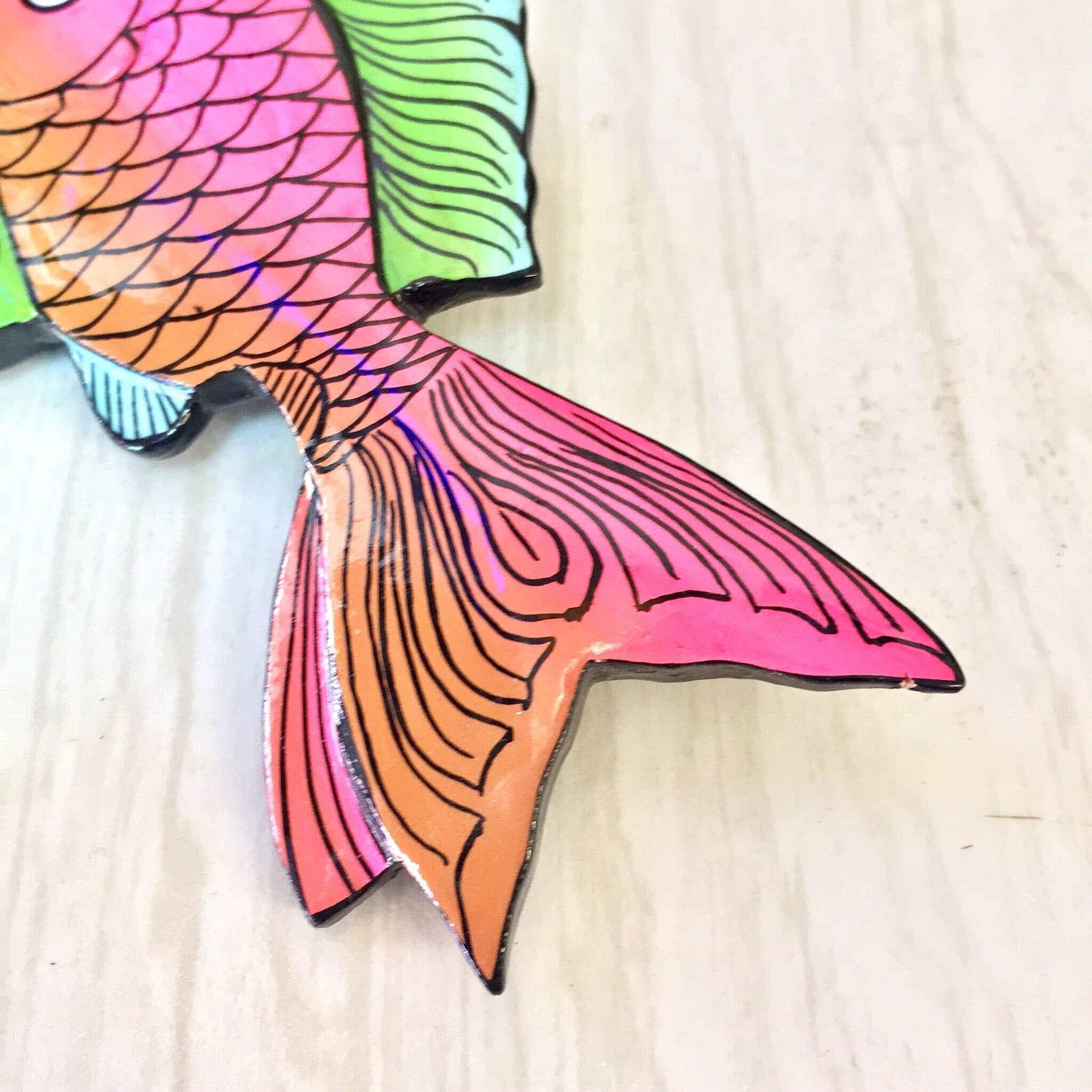 Large colorful wooden fish brooch pin in pink, orange, green and blue hues, featuring scale and fin details, vintage jewelry piece on light wood background.