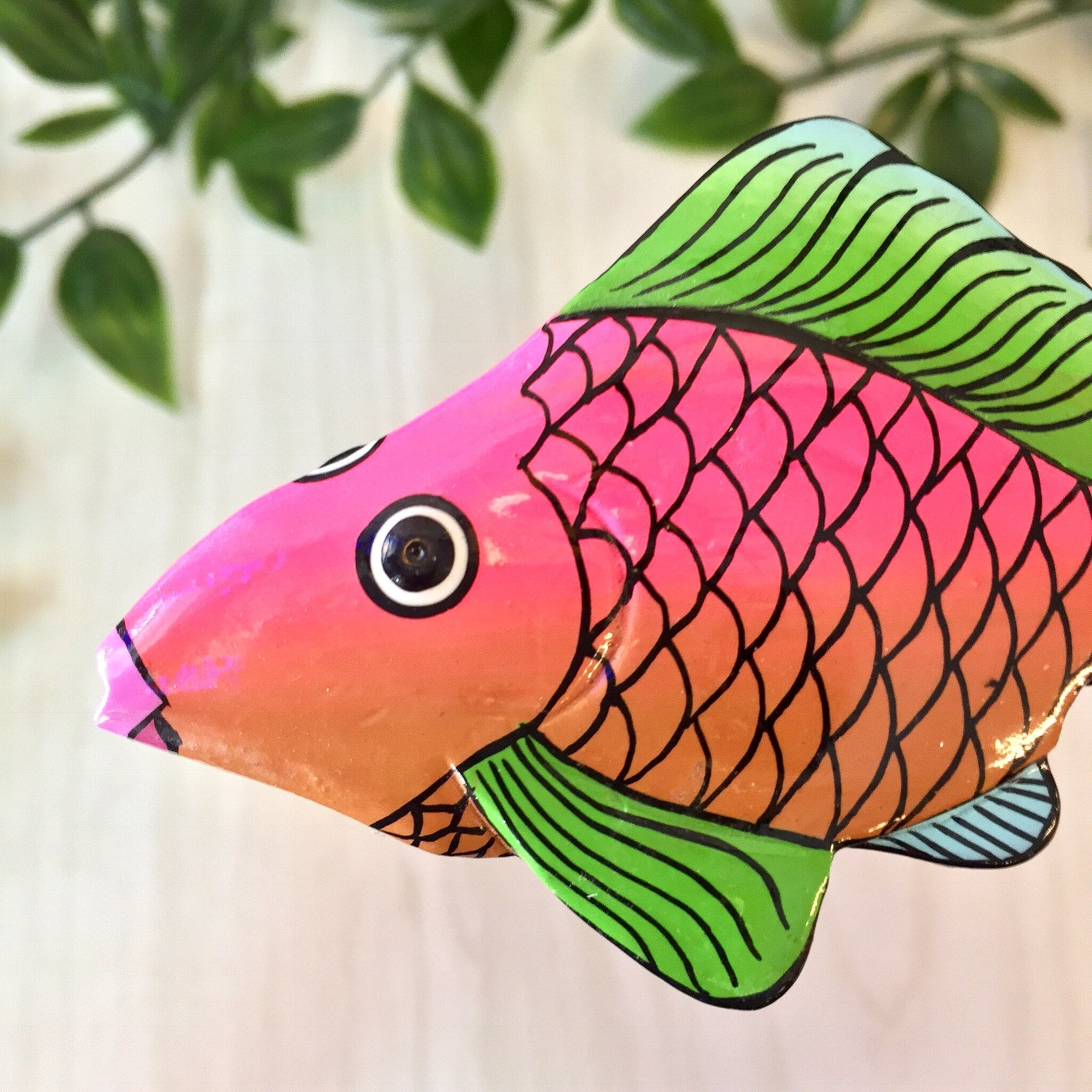Colorful vintage wooden fish brooch pin featuring pink, orange, green and blue colors against a leafy background.