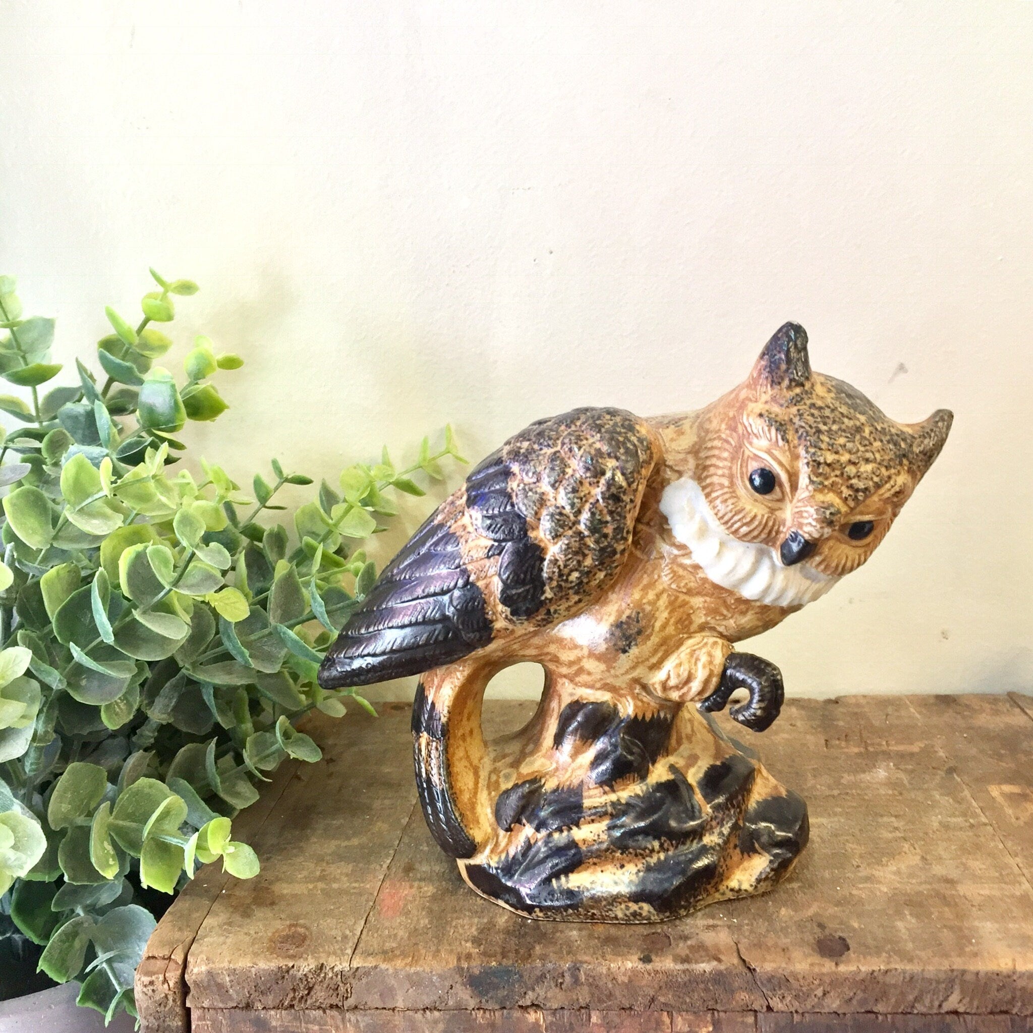 Vintage ceramic owl figurine with brown and black coloring, positioned next to green foliage on a wooden surface, perfect for home decor or as a Mother's Day gift.