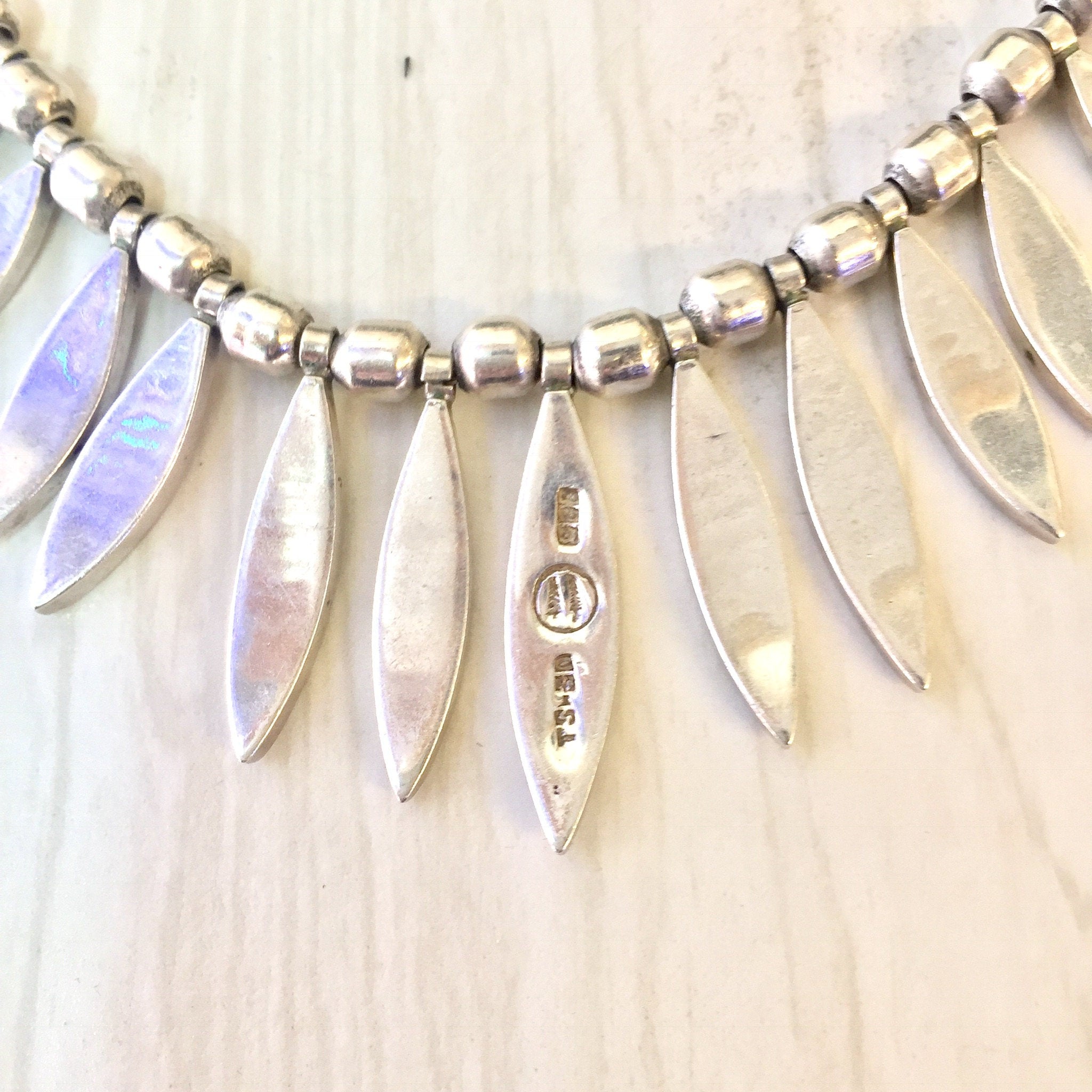 Vintage sterling silver bib necklace with dangling feather-shaped pendants in iridescent colors, creating a bold statement piece of Mexican jewelry suitable as a gift.